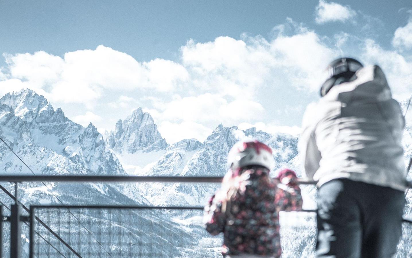 Ein Mann und ein Kind in Skikleidung blicken auf die Dolomiten