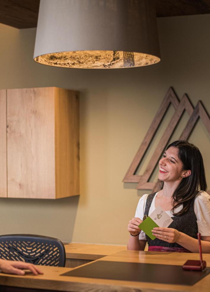 Eine Mitarbeiterin an der Hotelrezeption spricht freundlich mit einer ankommenden Besucherin