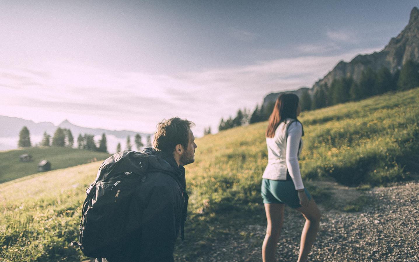 Un uomo e una donna fanno un’escursione, circondati da un ampio paesaggio di malga