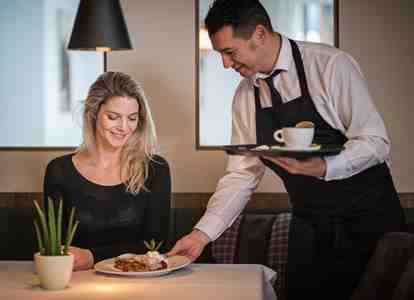 A woman is sitting at a set table while a waiter is serving her a cup of coffee