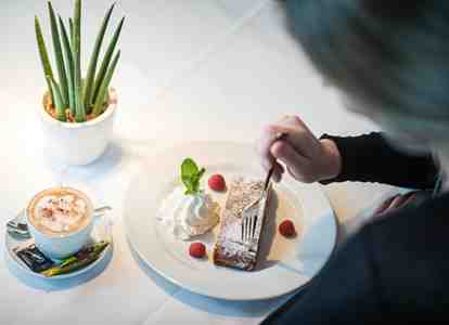Una donna è seduta a un tavolo, mangia uno strudel di mele e beve un cappuccino