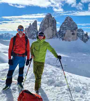 Due sciatori in primo piano, sullo sfondo le Tre Cime di Lavaredo