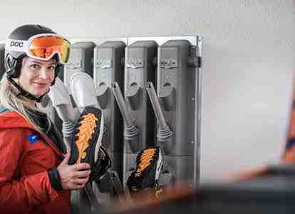 A woman in ski gear is taking a pair of ski boots from a ski locker