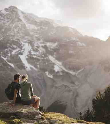 A couple is sitting on a rock and looking at the Dolomites