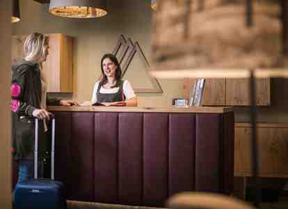 Eine Mitarbeiterin an der Hotelrezeption spricht freundlich mit einer ankommenden Besucherin