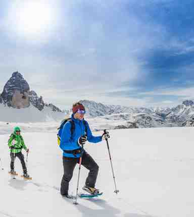 Eine Gruppe von Personen steigt mit Tourenskiern durch eine verschneite Berglandschaft, im Hintergrund die Drei Zinnen