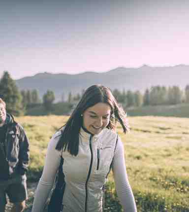 A man and a woman are hiking, surrounded by a wide alpine pasture landscape